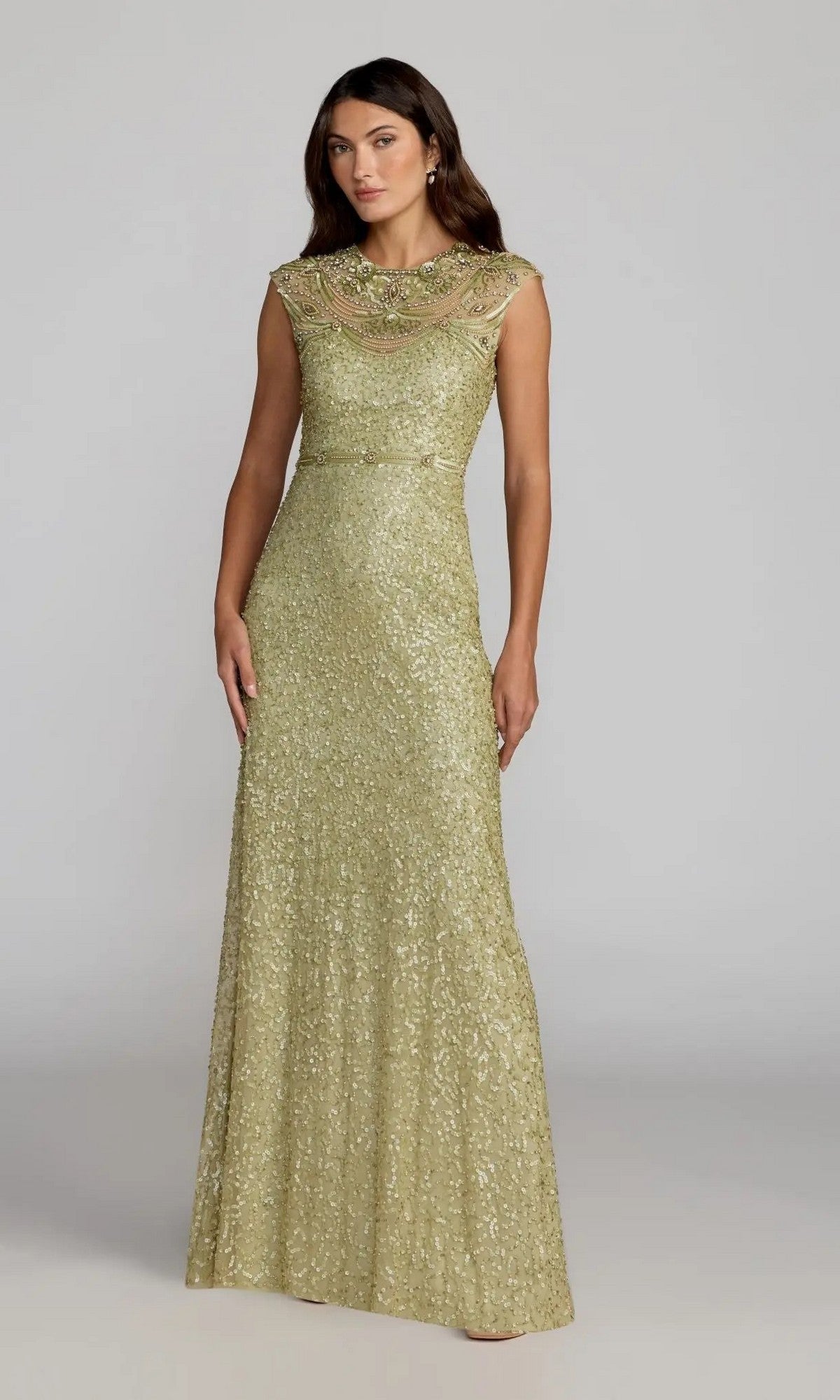 A woman wearing the Mac Duggal 23095 long formal dress, featuring a floor-length gold sequin design with a beaded neckline, stands against a plain light gray background.